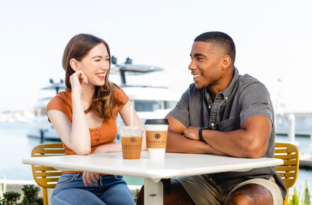couple smiling outside at a table at Portside Coffee and Gelato with the San Diego Bay in the background